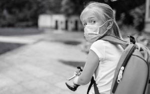 Young girl with mask rides her bike when school reopens during COVID-19